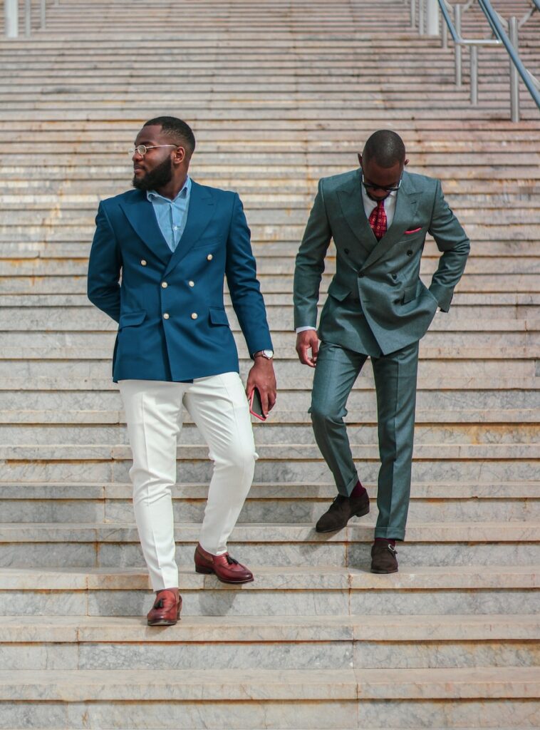 proud black man in blue coat and white pants standing beside proud black man in green coat